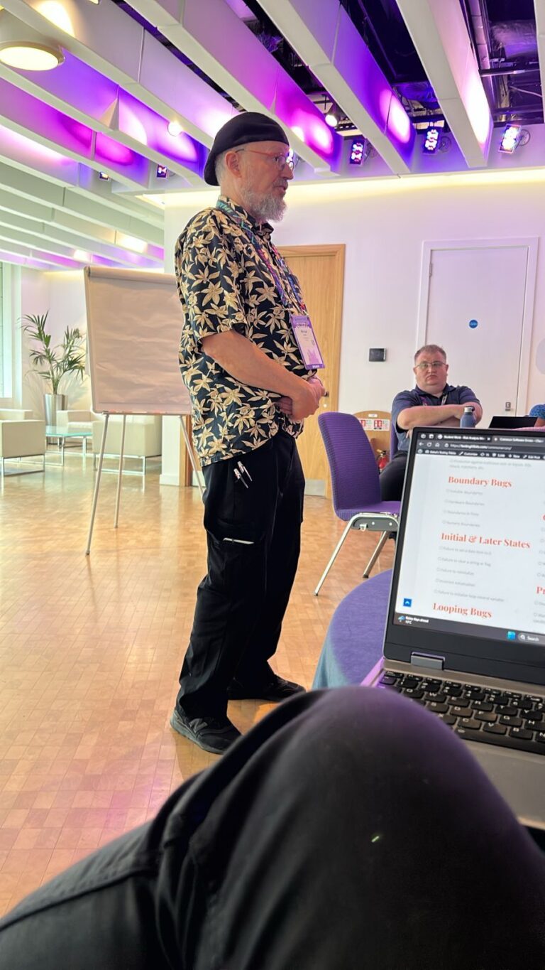 michal boltan giving a seminar, with a flip chart in the background and a laptop in the foreground displaying notes about software bugs.