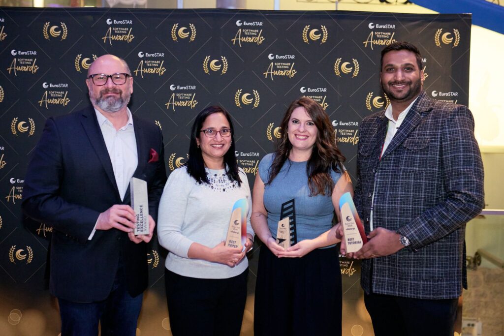Four smiling award recipients pose together at the EuroSTAR Software Testing Awards event, proudly holding their trophies in front of a branded backdrop celebrating achievements in the software testing community.